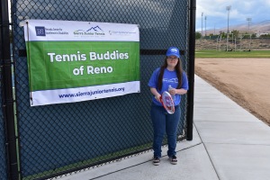 There is Tennis Buddies Sign say's Tennis Buddies of Reno and Jordan holding a tennis racket with ball in hand.